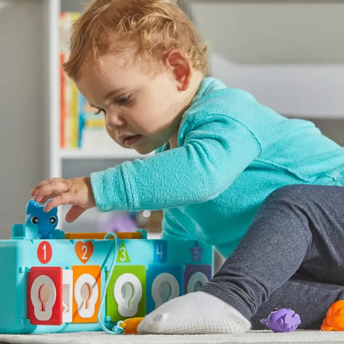 Toddler playing with a blue activity box featuring five numbered, colorful doors and pop-up animal figures.