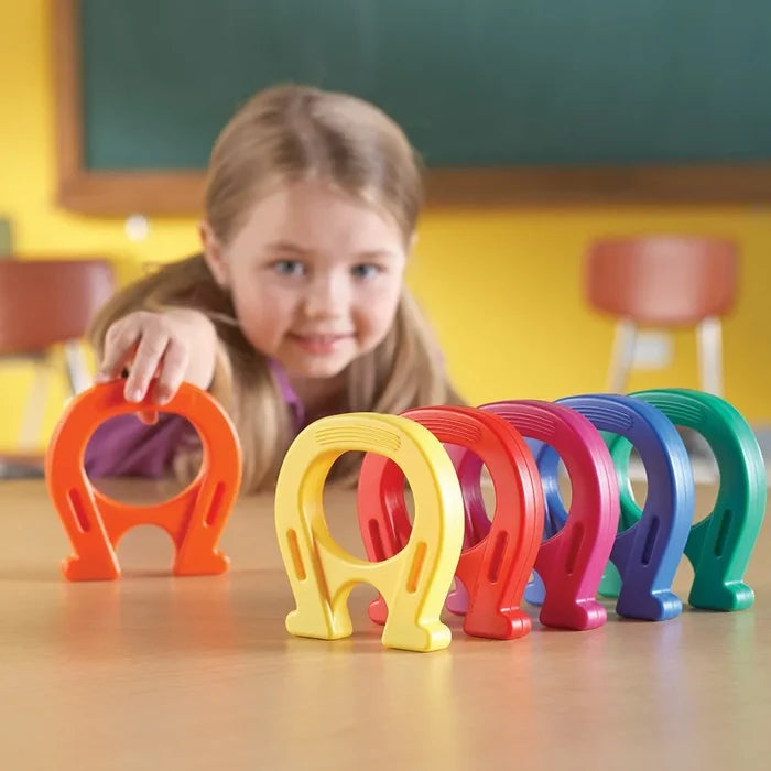 Child playing with large horseshoe-shaped magnets in orange, yellow, red, pink, blue, and green.