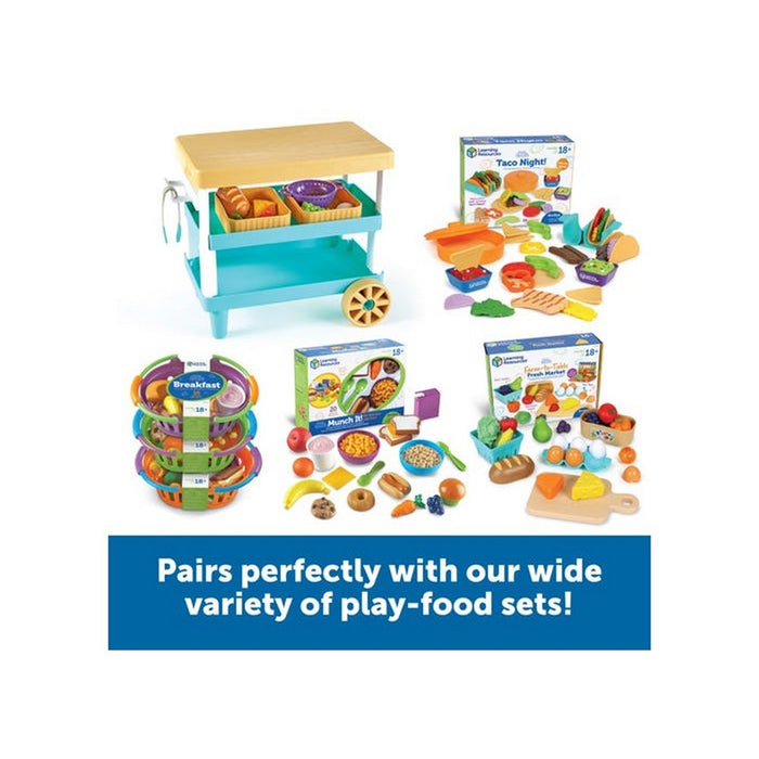 Light blue toy kitchen island with a tan top, surrounded by several colorful play food sets and storage baskets.