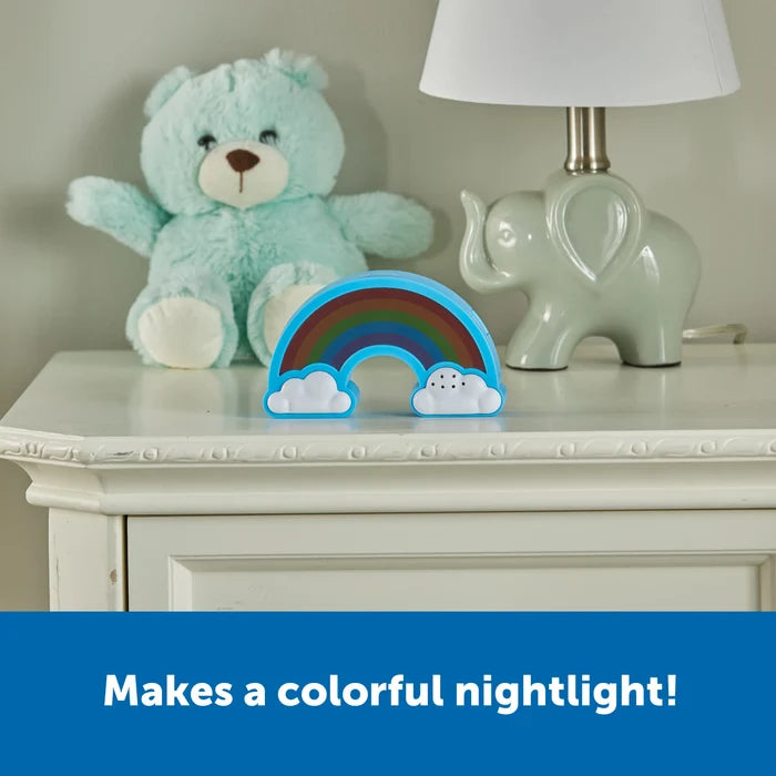 Blue rainbow-shaped timer with white clouds on a white nightstand next to a teddy bear and elephant lamp.