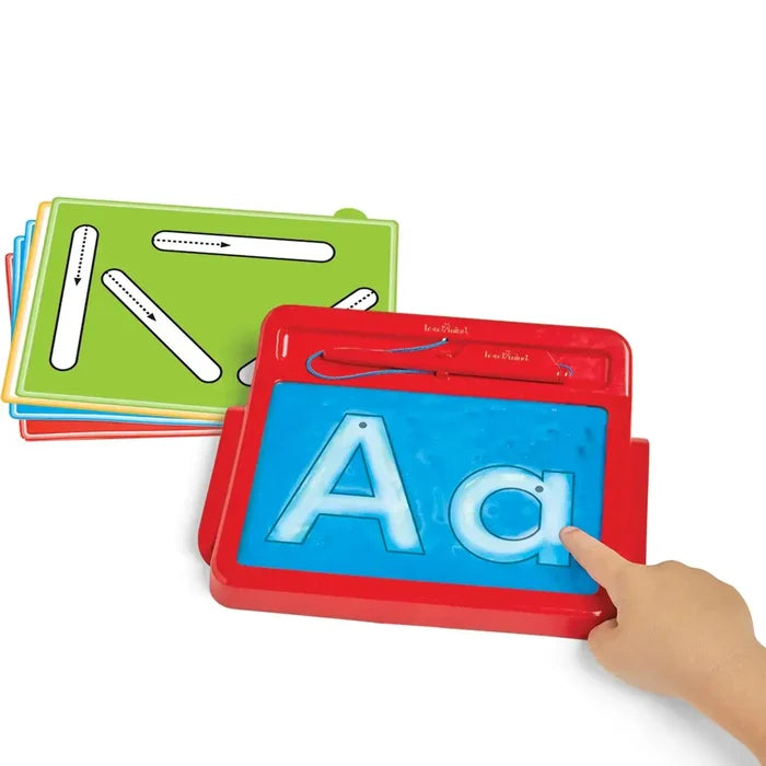 A hand traces Aa on a blue gel sensory pad in a red frame with colorful tracing cards in the background.