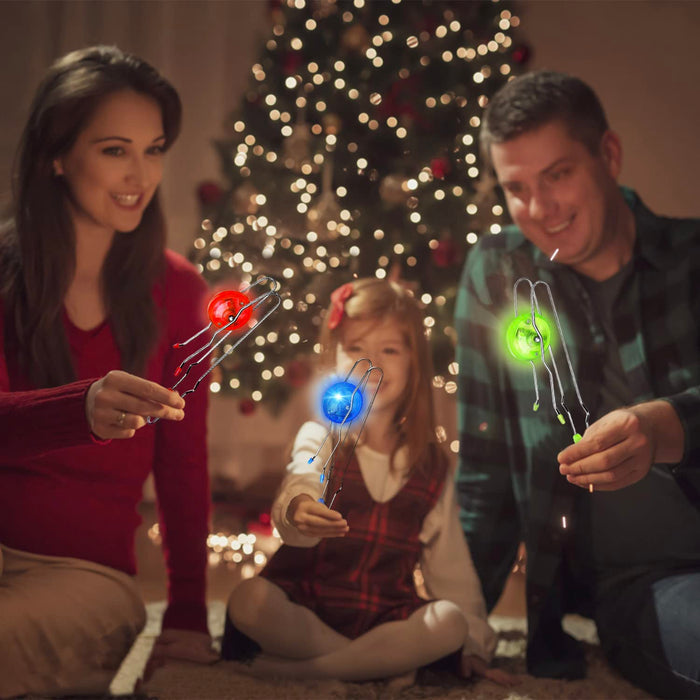 Family holding glowing red, blue, and green magnetic wheels spinning on wire tracks in front of a Christmas tree.