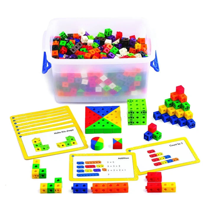 Clear tub of colorful linking cubes with yellow activity cards and built 3D shapes on a white background.