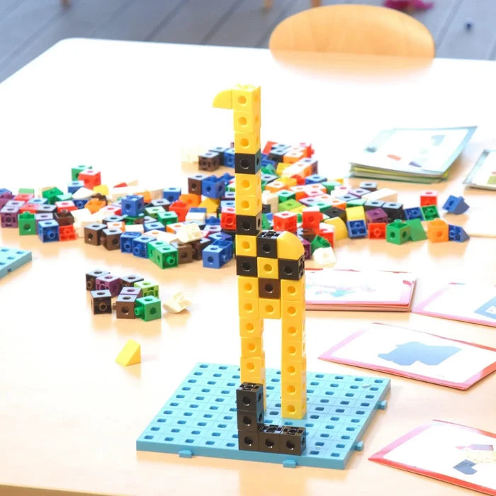 Multi-colored linking cubes with a tall yellow and black giraffe model built on a blue baseplate among loose blocks.