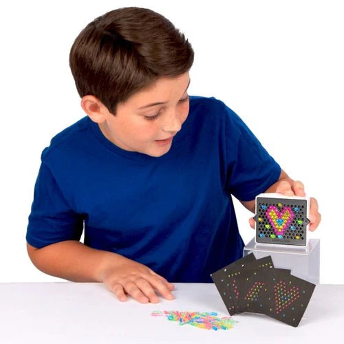 Boy in a blue shirt playing with a mini square light-up board showing a heart, with pegs and template cards.