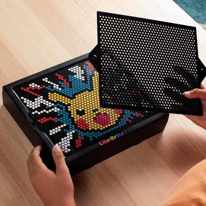 Lite-Brite toy displaying a glowing Pikachu design with colorful pegs as a hand holds a black perforated grid over it.