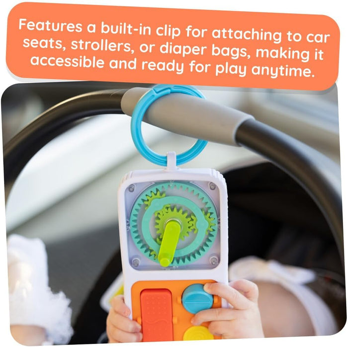 White baby activity toy with green gears and orange buttons attached to a car seat handle by a blue plastic clip.