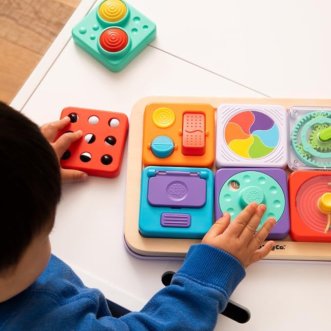Toddler playing with a wooden sensory board featuring colorful interactive modules with buttons, gears, and switches.