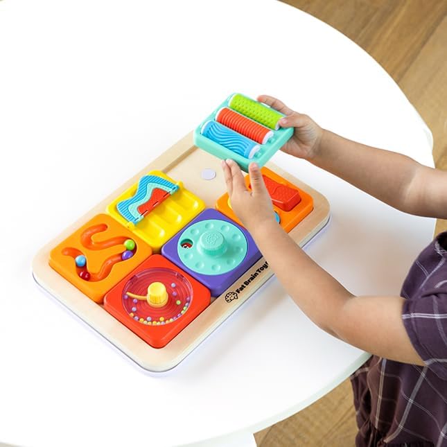 A child plays with a wooden sensory board featuring colorful, textured, and movable plastic tiles and components.