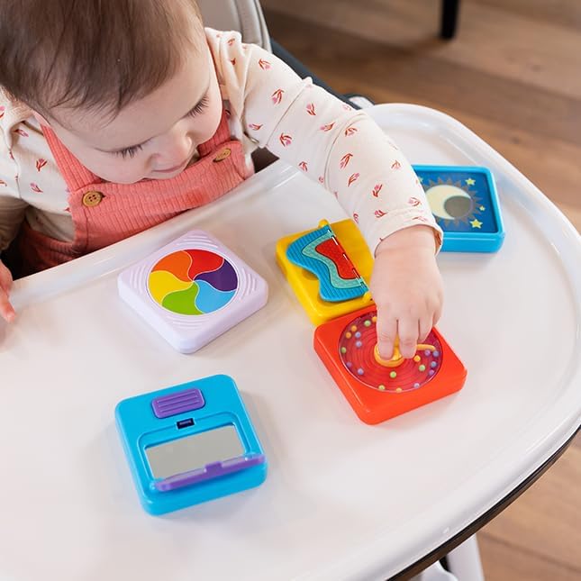 A baby plays with colorful square activity tiles featuring a mirror, rainbow spinner, and bead maze on a white tray.