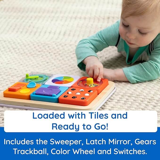 Baby playing with a wooden activity board featuring six colorful sensory tiles with gears, switches, and a trackball.