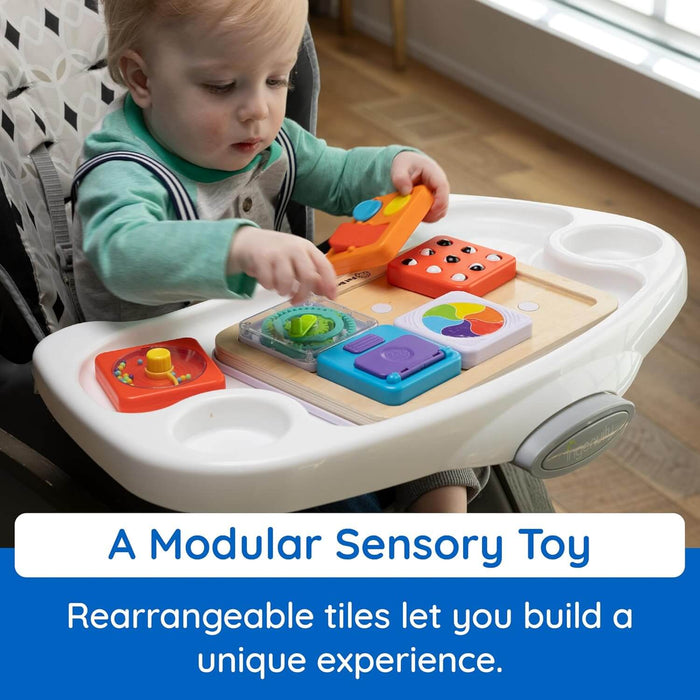 Toddler playing with a wooden sensory board featuring colorful, interchangeable activity tiles on a high chair tray.