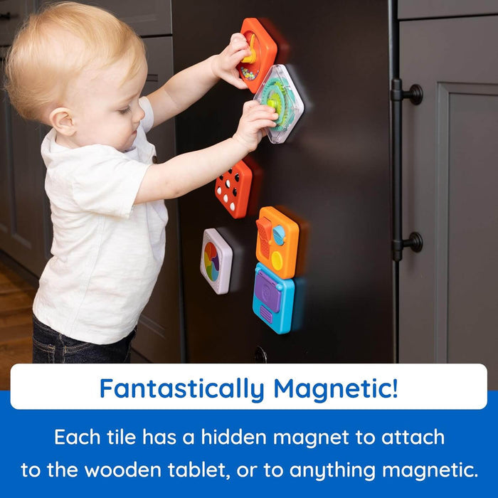 A toddler sticks colorful geometric magnetic activity tiles to a black refrigerator door.