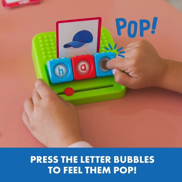 Child pressing colorful letter blocks in a green tray to spell cap, matching a blue baseball hat picture card.