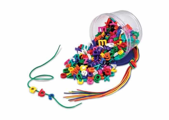 Colorful plastic lowercase letter beads spill from a clear jar next to vibrant laces and 'abc' on a green string.
