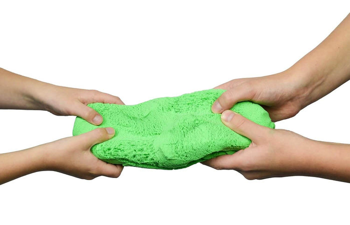 Two sets of hands pull and stretch a bright green, textured lump of modeling dough against a white background.
