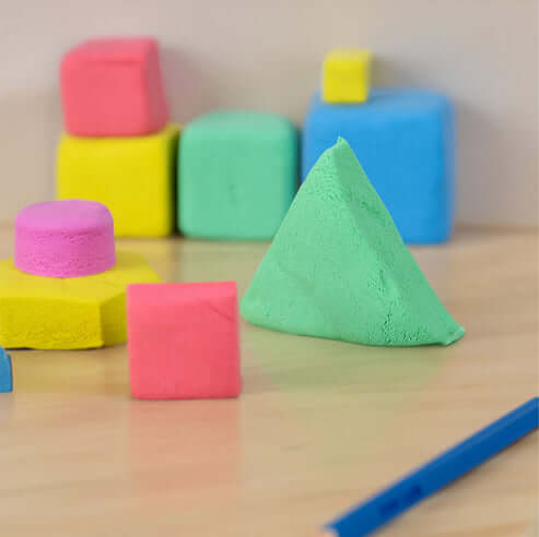 Pink, yellow, blue, and green geometric blocks and a pyramid molded from soft, colorful modeling dough.