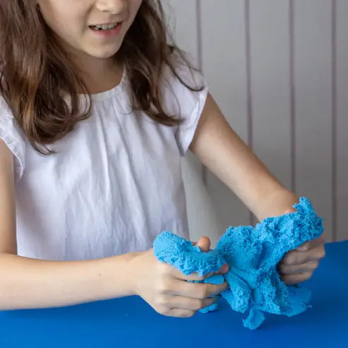 A girl stretches and molds vibrant blue, textured modeling dough with her hands.