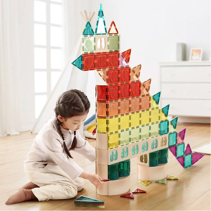 Young girl building a large dragon with colorful translucent magnetic tiles and curved wooden-style base pieces.