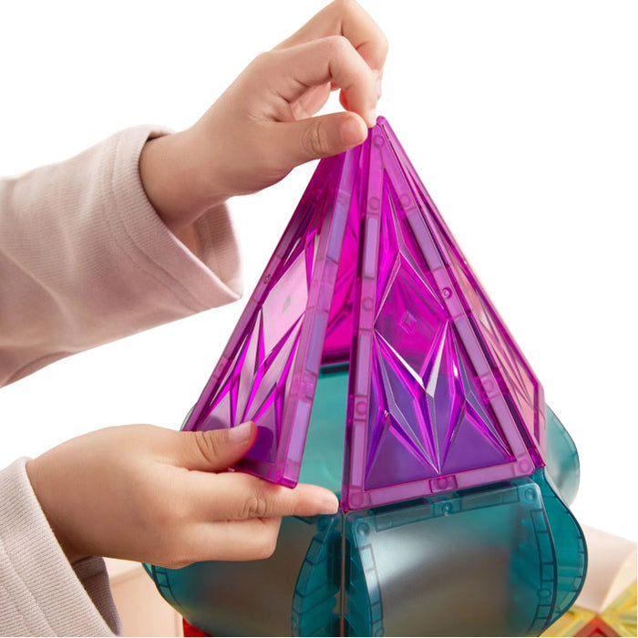 Child's hands building a tower with translucent purple triangular and teal curved magnetic tiles.