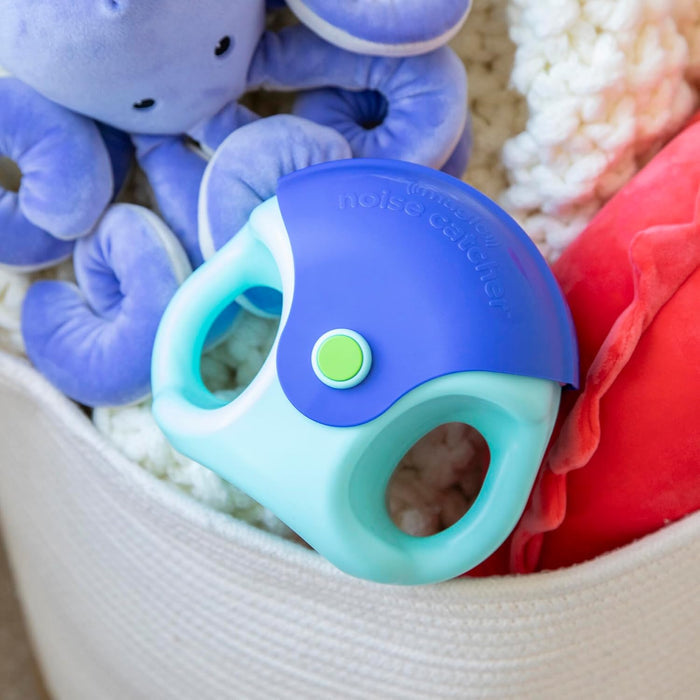 Handheld blue and turquoise plastic toy with a green button, sitting in a woven basket with plush toys.