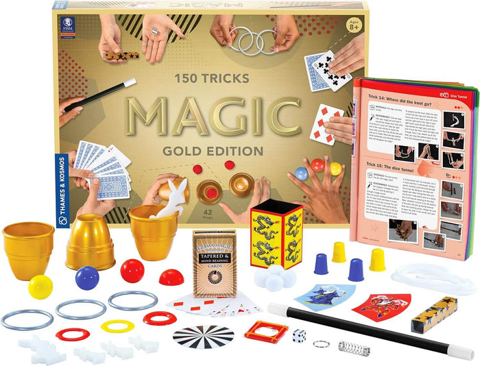 Magic kit box with gold cups, a wand, cards, and rings displayed around an open instruction book.