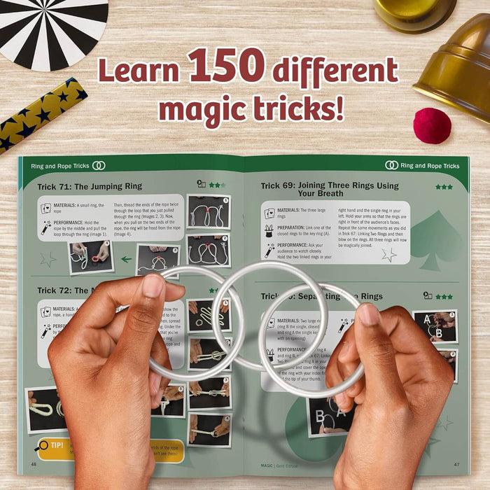 Hands holding two silver rings over an open instruction book with magic props on a wooden surface.