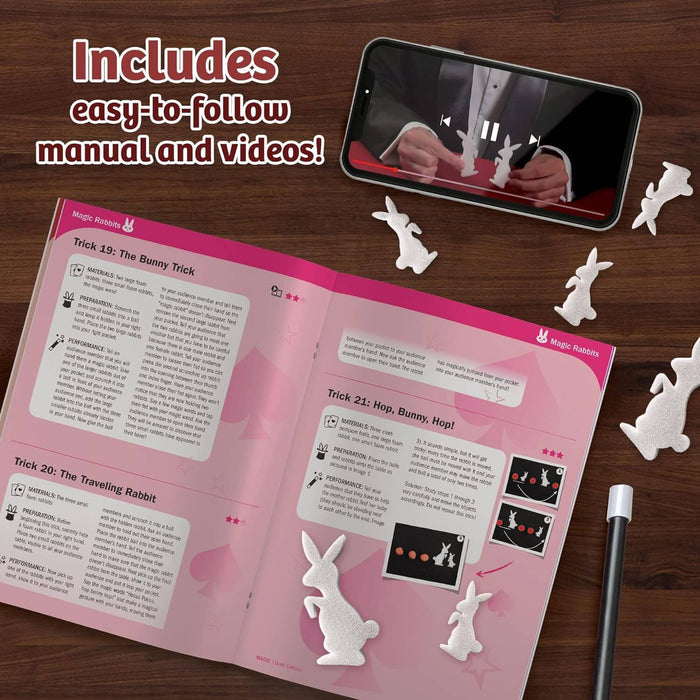 Magic manual, small foam rabbits, and a phone showing a video tutorial on a wooden surface.