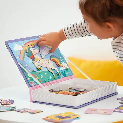 Child places magnetic unicorn pieces on a colorful rainbow scene inside a purple book-shaped storage box.