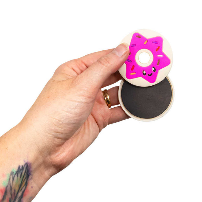 Hand holding two round magnetic toy discs: one white with a pink star donut face and one with a black magnet center.