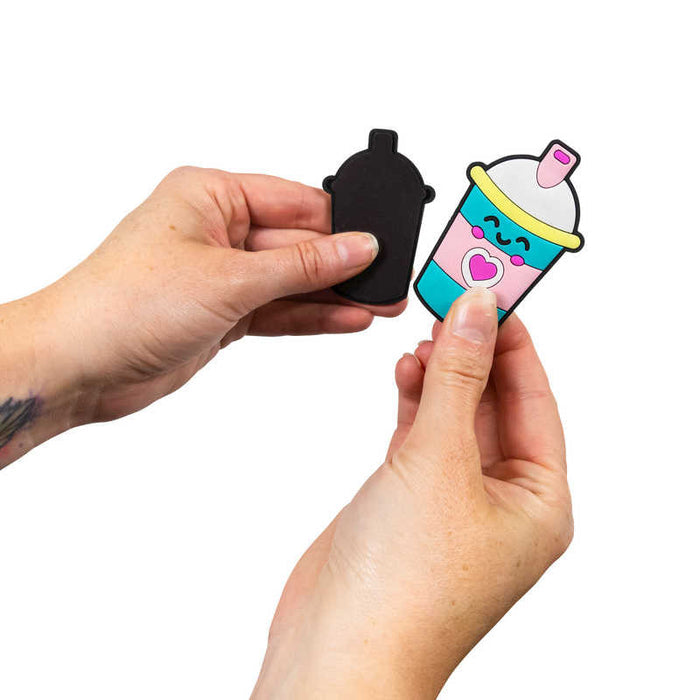 Hands holding a black base and a colorful cartoon milkshake cup with a pink heart, smiley face, and teal stripes.