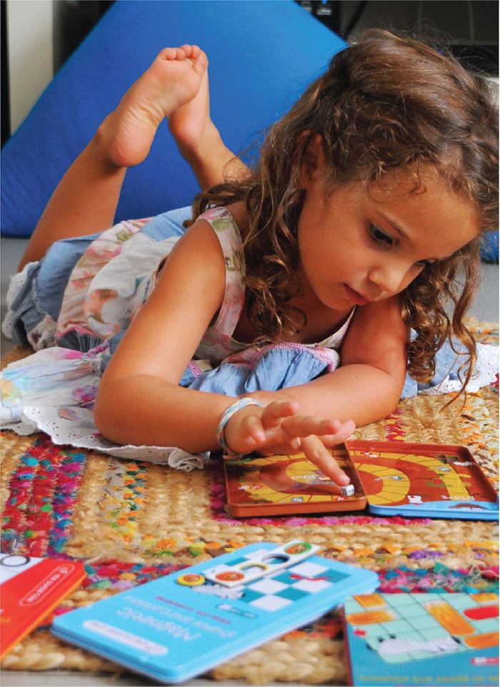 Young girl playing with compact magnetic travel games in colorful metal tins on a textured woven rug.