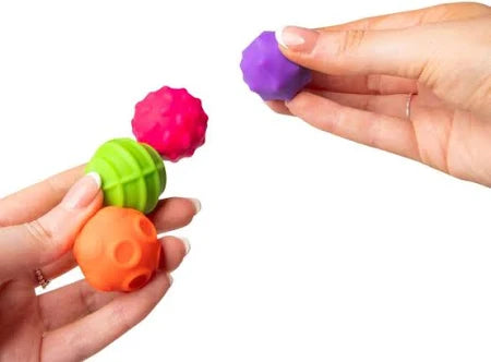 Hands holding four colorful textured spheres in purple, pink, green, and orange.