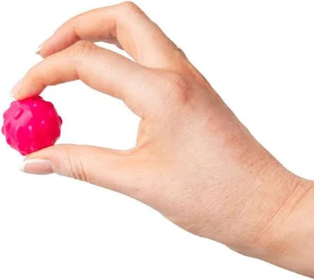 A hand holding a small, bright pink textured sensory sphere between the thumb and index finger.