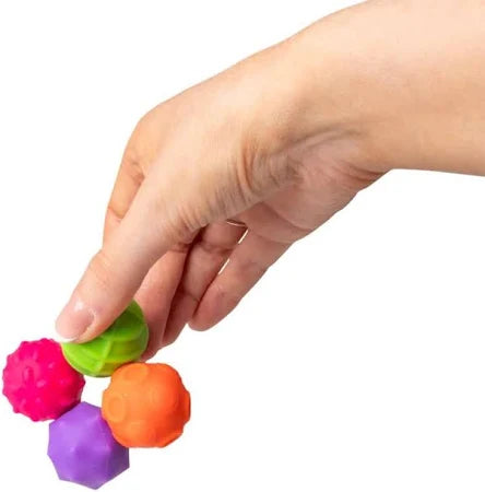 Hand holding four small, textured magnetic spheres in pink, orange, green, and purple.