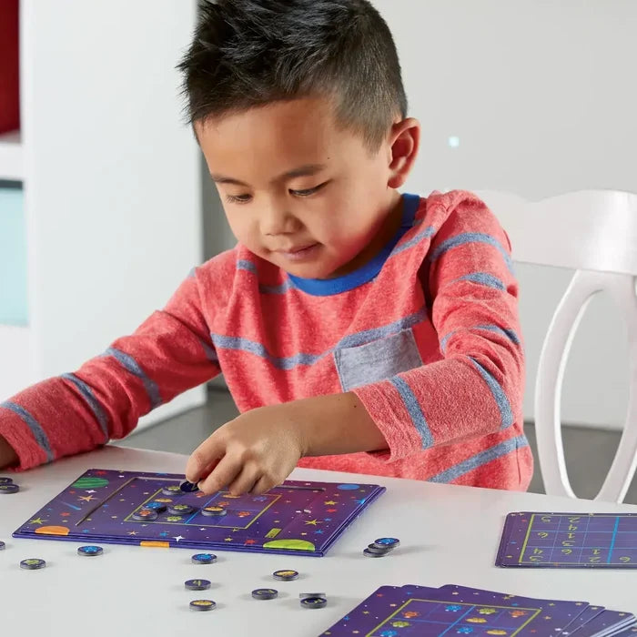 Child playing a purple space-themed magnetic sudoku board game with round tokens and galaxy illustrations.