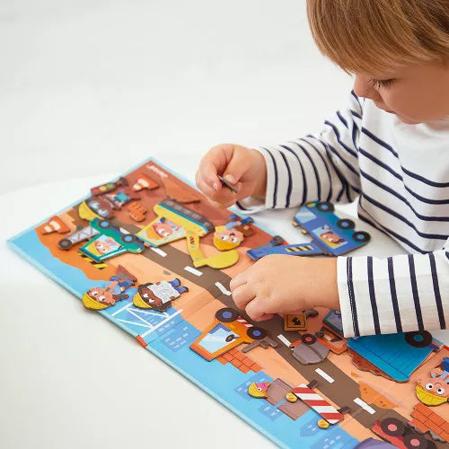 Child in a striped shirt placing colorful magnetic construction vehicles and workers on a fold-out activity board.