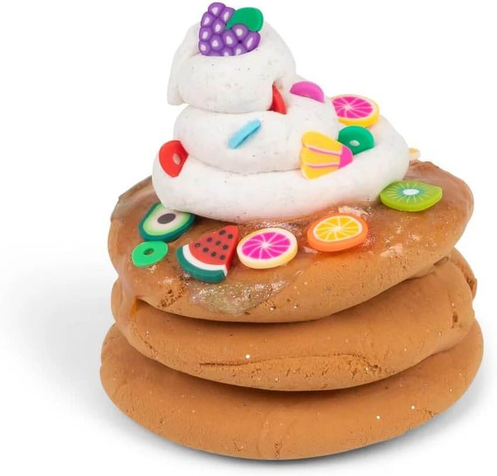 Stack of three brown putty pancakes topped with a white slime swirl and colorful miniature fruit charms.