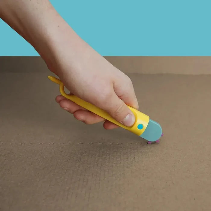 Hand using a yellow plastic tool with a purple spiked wheel to score a perforated line on brown cardboard.