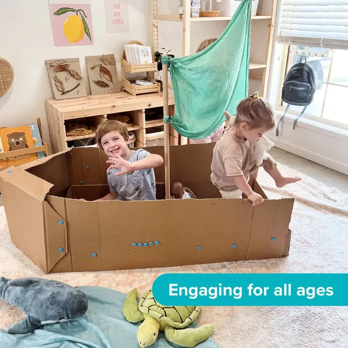 Two children playing in a large cardboard boat built with blue plastic fasteners and a teal sail in a bright playroom.