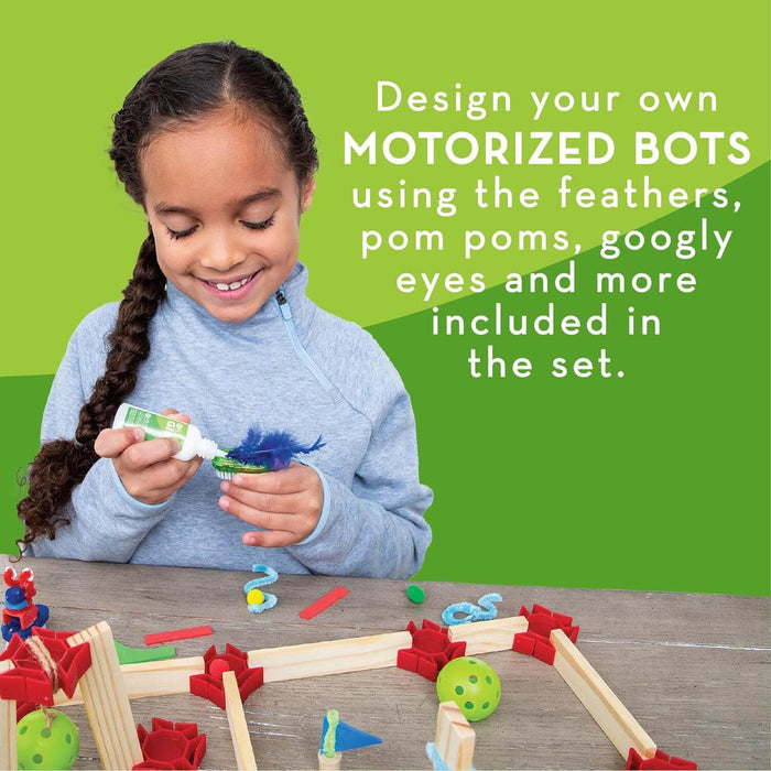 A girl glues a blue feather to a small bot over a wooden maze with colorful craft supplies on a green background.