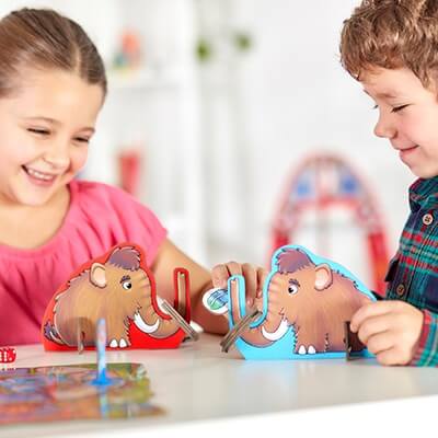 Two children playing with red and blue mammoth cardboard standees and rings over a colorful patterned game board.