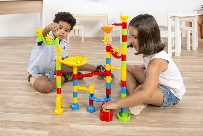 Two children playing with a colorful marble run featuring bright tubes, funnels, and spinning wheels.