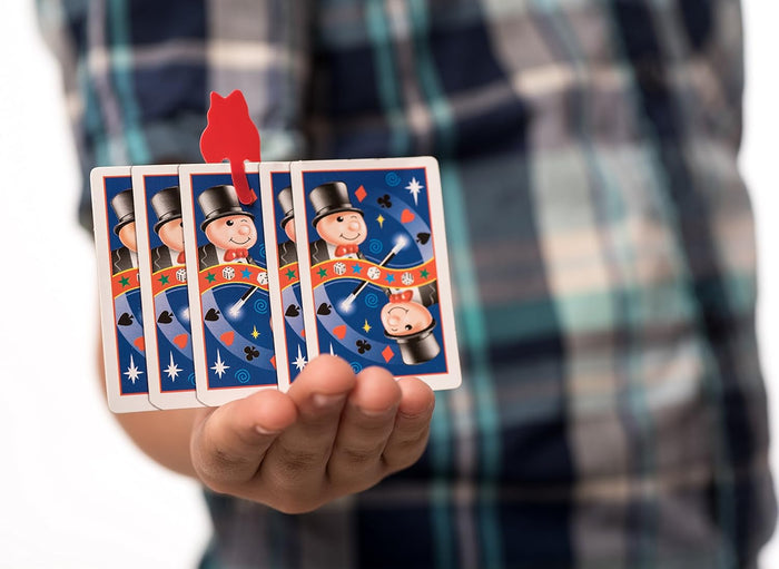 Child holding a fan of five magician-themed playing cards with a red cat-shaped plastic clip on the center card.