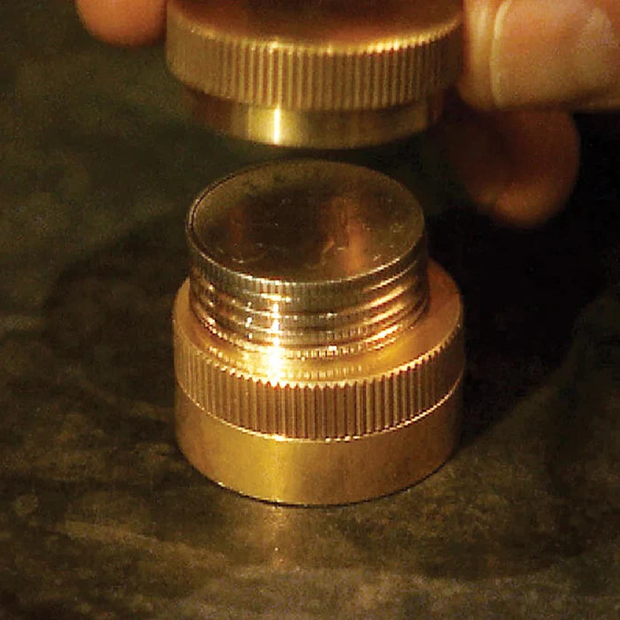 Fingers lower a knurled brass cap over a stack of silver coins sitting in a matching brass base.