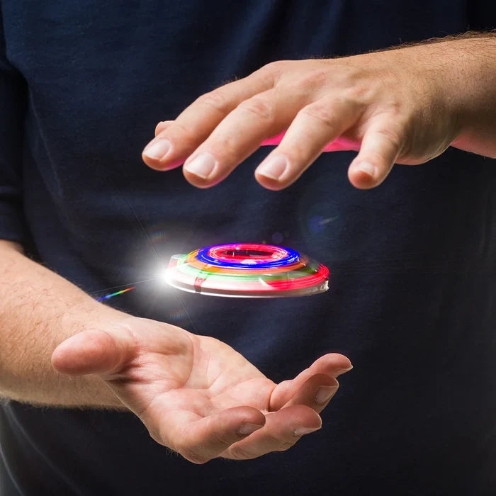 A spinning saucer toy with glowing red and blue LED rings appears to levitate between a person's open hands.