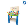 Wooden toy workbench with blue legs, green front, pegboard with gears, and colorful play tools and accessories.