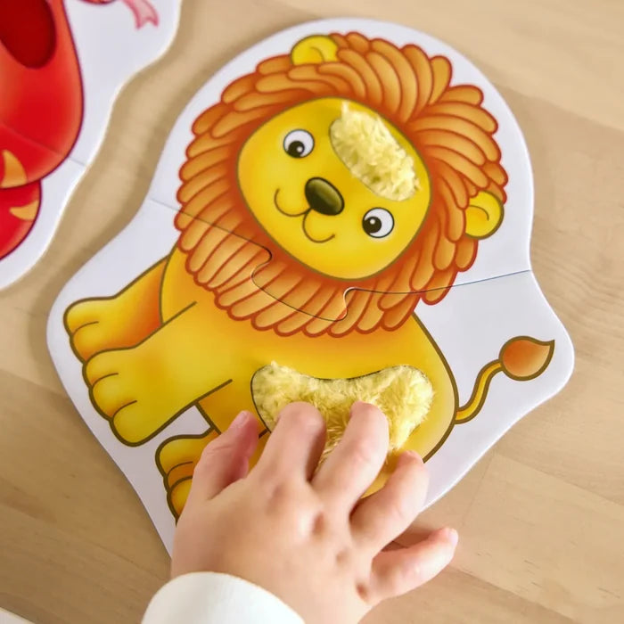 Toddler's hand touching fuzzy textured patches on a yellow and orange lion puzzle with two interlocking pieces.