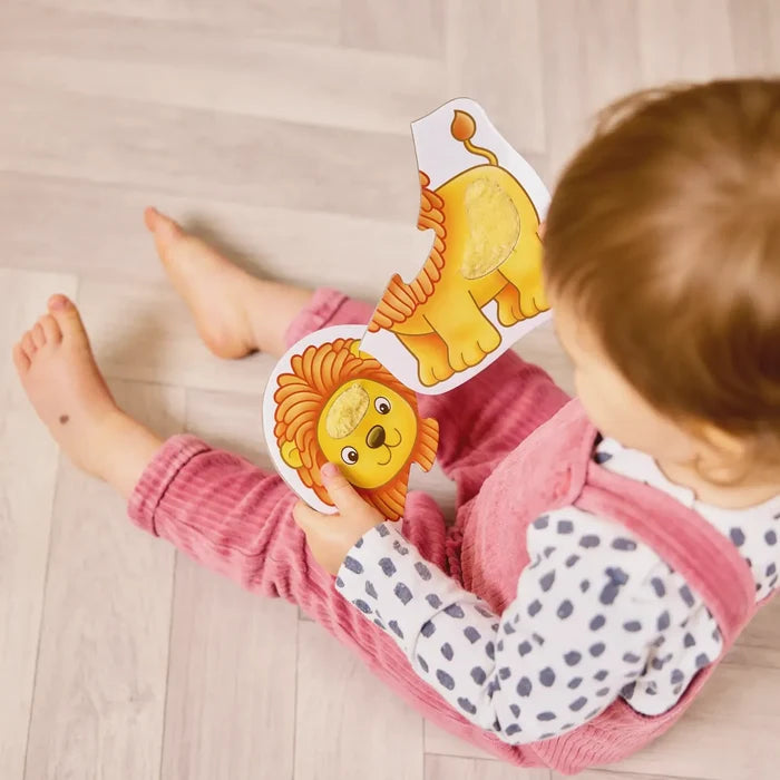Toddler holds two large puzzle pieces forming a yellow lion with fuzzy textured inserts on a light wood floor.