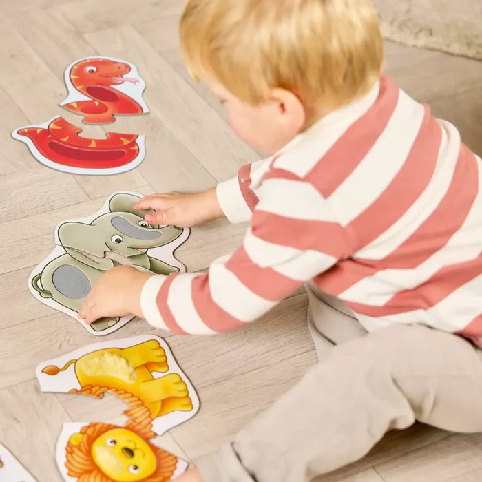 Toddler assembling textured two-piece puzzles of a red snake, green elephant, and yellow lion on a wooden floor.